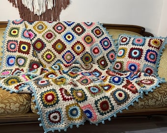 May include: A colorful crocheted throw blanket with a granny square pattern in shades of red, blue, green, yellow, and pink. The blanket is draped over a couch with a matching pillow.