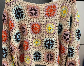 May include: A crocheted sweater with a square pattern in shades of brown, pink, blue, yellow, and white.