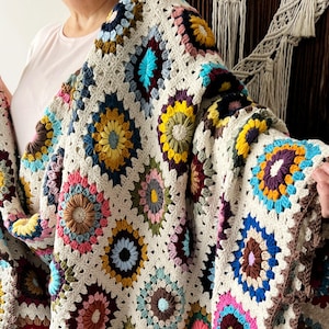 May include: A crocheted throw blanket with a granny square pattern featuring colorful circles in shades of pink, blue, green, yellow, and brown.