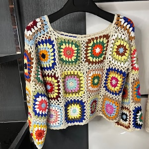 Op de afbeelding: Een kleurrijk gehaakt topje met een vierkant patroon. Het topje is gemaakt van verschillende kleuren, waaronder rood, oranje, geel, groen, blauw en paars.