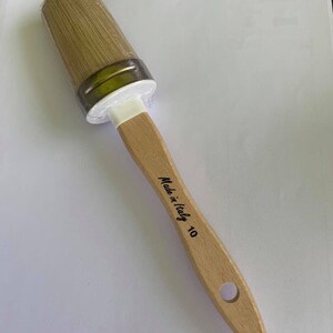 May include: A new, unused paintbrush with a light wooden handle and natural bristles. The brush head is oval-shaped and wrapped in clear plastic. The handle is stamped with "Made in Italy 10".