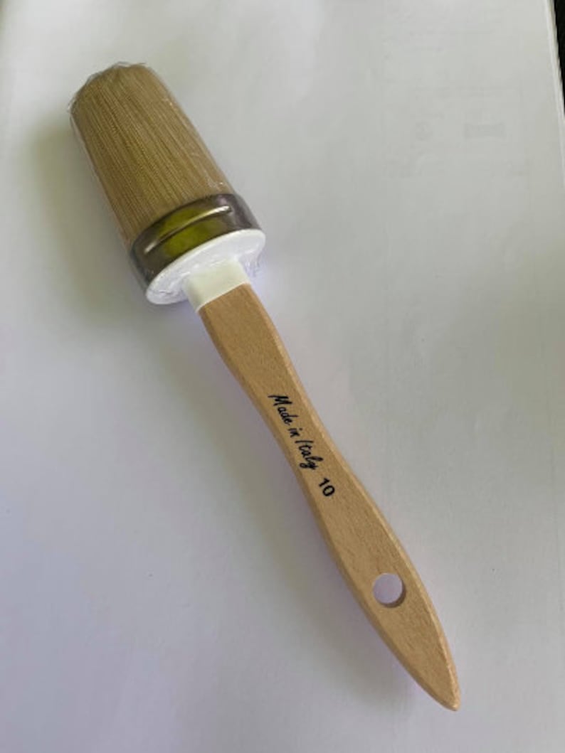 May include: A new, unused paintbrush with a light wooden handle and natural bristles. The brush head is oval-shaped and wrapped in clear plastic. The handle is stamped with "Made in Italy 10".