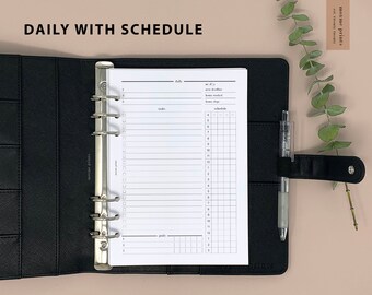 May include: A black leather bound planner with silver rings and a white daily planner insert. The insert has sections for daily tasks, goals, and a schedule.