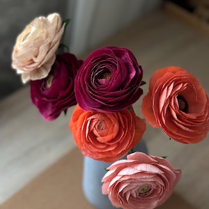 May include: A bouquet of paper flowers in a vase. The flowers are in shades of pink, orange, and red.