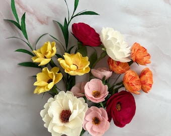 May include: A bouquet of handcrafted crepe paper flowers featuring a variety of colors including deep red, cream, soft pink, bright yellow, and orange-streaked petals. The arrangement includes green paper leaves and stems on thin wire supports.