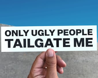 May include: A white rectangular sticker with the text "ONLY UGLY PEOPLE TAILGATE ME" in black, held up against a blue sky and a gray concrete surface.