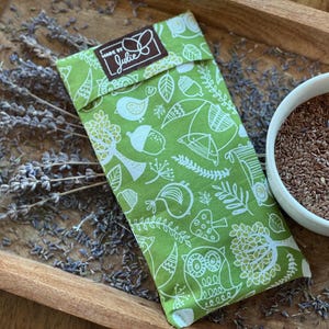 May include: A green fabric pouch with a white woodland pattern, including birds, owls, and acorns, rests on a wooden tray with dried lavender and a bowl of seeds. The pouch has a label that says "Made by Julie".