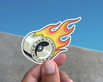 May include: A white sticker with a wheel on fire. The wheel has the text "Ride Fast or Go Home" on it.