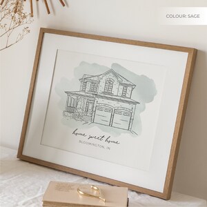 K&ouml;nnte beinhalten: Eine gerahmte Illustration eines Hauses mit einem salbeigr&uuml;nen Aquarellhintergrund. Das Haus ist in schwarzer Tinte gezeichnet und hat ein Garagentor. Der Text "home sweet home BLOOMINGTON, IN" ist unter dem Haus gedruckt.