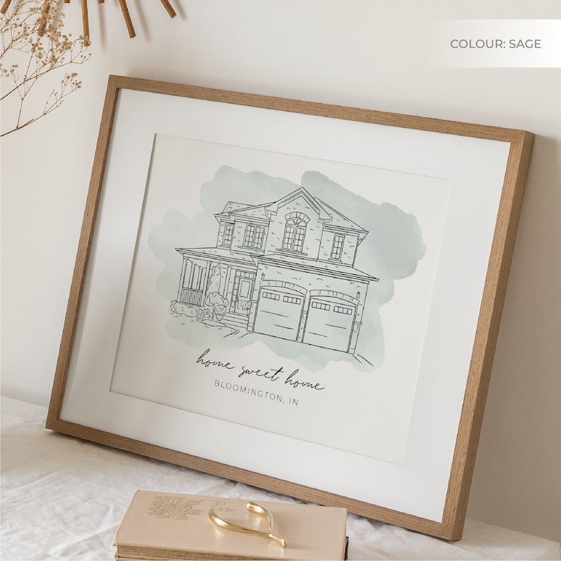 K&ouml;nnte beinhalten: Eine gerahmte Illustration eines Hauses mit einem salbeigr&uuml;nen Aquarellhintergrund. Das Haus ist in schwarzer Tinte gezeichnet und hat ein Garagentor. Der Text "home sweet home BLOOMINGTON, IN" ist unter dem Haus gedruckt.