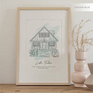 K&ouml;nnte beinhalten: Eine gerahmte Illustration eines Hauses mit einem blauen Aquarellhintergrund. Der Text unter dem Haus lautet "Lake Tahoe, The Young Family Holiday, Winter 2022". Der Rahmen ist aus hellem Holz.