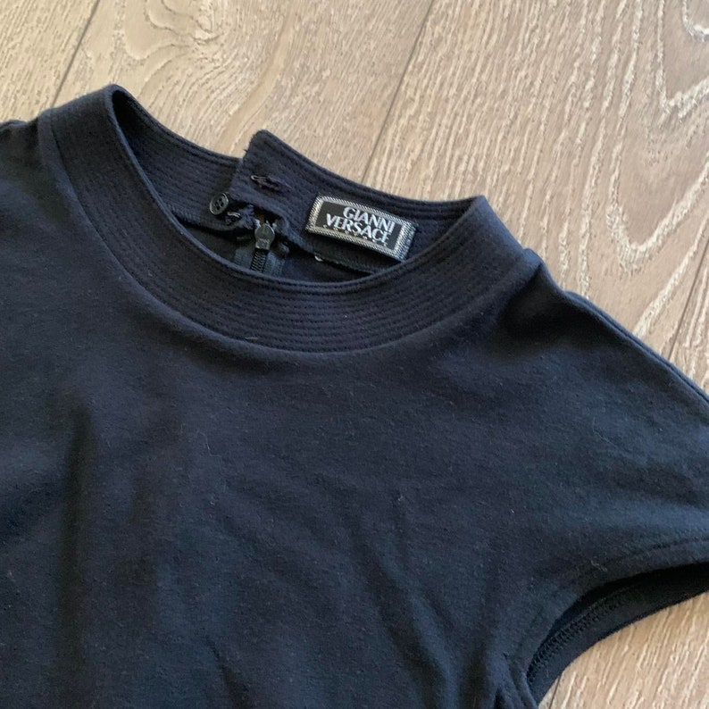 May include: Black short-sleeved shirt with a black zipper and a black label that reads "Gianni Versace" on the back of the collar.