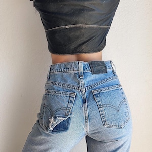 May include: A pair of light blue denim jeans with a distressed patch on the back pocket. The jeans have a silver tab with the text "Silver Tab" on the back waistband.