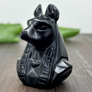 Puede incluir: Estatua de Anubis de obsidiana negra con una talla detallada del dios egipcio. La estatua mide aproximadamente 10 cm de alto y está hecha de obsidiana negra pulida.