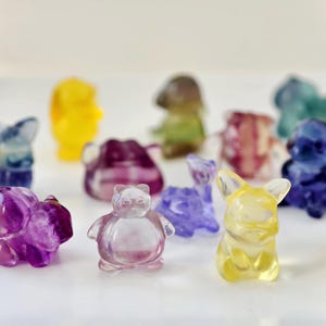 May include: A collection of colorful, translucent animal figurines in various shapes, including a dog, bear, and bird. The figurines are in shades of purple, yellow, blue, and green, with a glossy finish. The background is plain white.