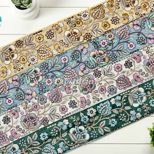 Puede incluir: Cinco cintas de adorno bordadas diferentes con motivos florales en tonos de verde, azul, rosa y amarillo. Las cintas están dispuestas en fila sobre una superficie de madera blanca.