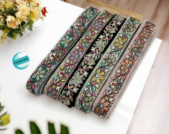 May include: Five different embroidered trim ribbons with floral designs in various colors, including green, pink, yellow, and blue. The ribbons are arranged in a row on a white surface.