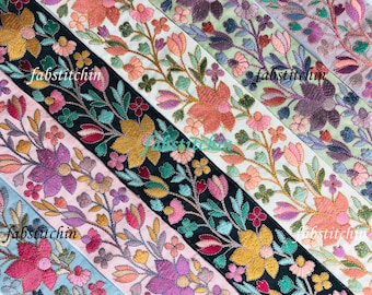 May include: Five different embroidered trim ribbons with floral designs in shades of pink, purple, green, blue, and gold. The ribbons are arranged in a diagonal pattern with the text "fabstitch.in" visible on each ribbon.