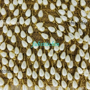 May include: White pearl beads sewn onto a gold fabric trim. The beads are teardrop shaped and are arranged in rows. The fabric trim is a delicate, open weave.