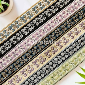 Può includere: Cinque diversi bordi di nastro di tessuto ricamato con un motivo a foglie. I bordi sono in tonalità di verde, crema, viola, nero e blu.