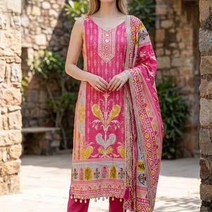May include: A sleeveless pink tunic and matching pants set with a patterned scarf. The tunic features a V-neck and intricate embroidery. The scarf has a decorative border with tassels. The outfit is a vibrant and stylish ensemble.