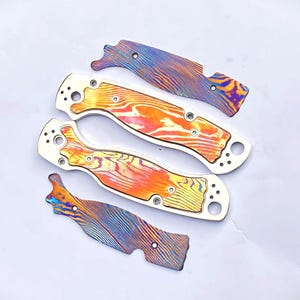 May include: Four custom knife scales and liners. The scales have a vibrant orange, yellow, and red pattern, while the liners feature a blue, purple, and gold pattern. The scales are made of a durable material and are designed to fit a folding knife.