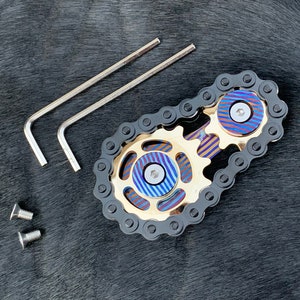 May include: A black chain links to two gold gears with blue and purple accents. The gears have a screw in the center. Two silver Allen wrenches and two silver screws are also included.