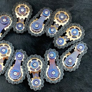 May include: A collection of 12 gold and black metal fidget toys shaped like bicycle chain links. Each link has a small gear and a blue and gold patterned bar.
