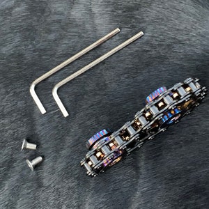 May include: A black metal chain fidget toy with two blue and purple colored metal rings. The toy comes with two allen wrenches and two screws.