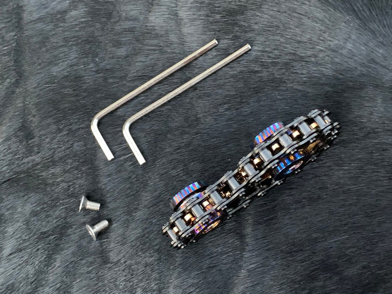 May include: A black metal chain fidget toy with two blue and purple colored metal rings. The toy comes with two allen wrenches and two screws.