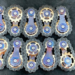 May include: Ten intricately designed metal fidget toys with a blue and gold finish. Each toy features a chain, a gear, and a rotating bar.