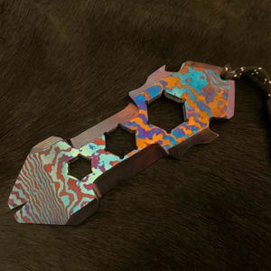 May include: A multi-tool with a blue, orange, and purple iridescent finish. The tool has a variety of shapes and sizes, including a hex wrench, a flathead screwdriver, and a bottle opener. The tool is attached to a black lanyard.
