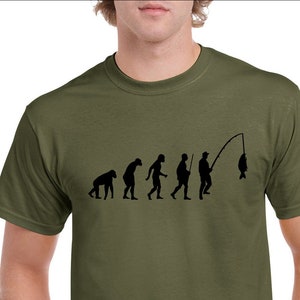 May include: A green t-shirt featuring a black graphic of the evolution of man, culminating in a man fishing. The graphic depicts a series of stick figures, starting with a monkey, then a caveman, then a man with a spear, and finally a man with a fishing rod and a fish.
