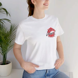 Può includere: T-shirt bianca con grafica rossa e nera sul petto. La grafica presenta un design di labbra rosse stilizzate con le parole "On My Worst Behavior" in un carattere script.