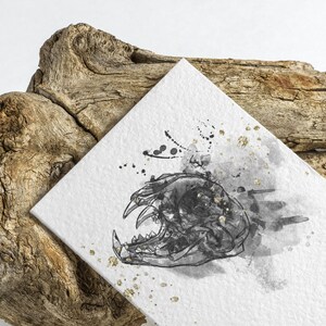May include: A black and white illustration of an animal skull with a watercolor background. The skull is drawn in a detailed style with sharp teeth and a prominent jaw. The background is a soft gray with hints of gold.