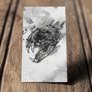 May include: A black and white illustration of a skull with an eye socket, set against a watercolor background with black and gold splatters.