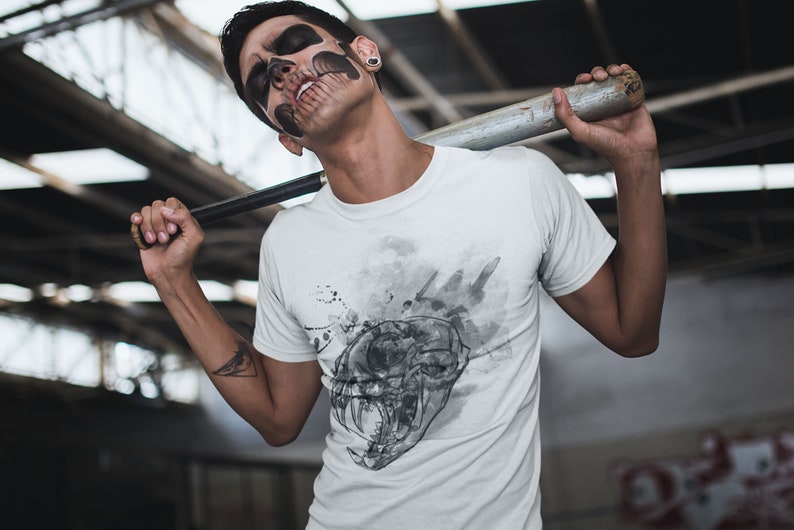 May include: A white t-shirt with a black and white graphic print of a skull with a watercolor effect. The skull has sharp teeth and is surrounded by black splatters.