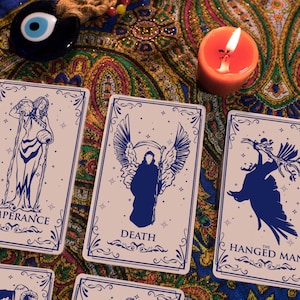 May include: Three tarot cards on a patterned fabric background. The cards are "Temperance", "Death", and "The Hanged Man". Each card features a blue silhouette on a light pink background with a decorative border.