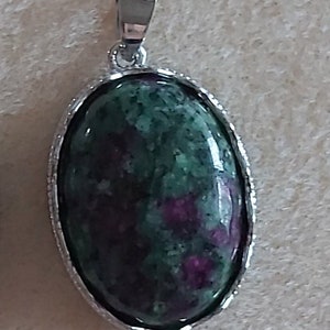 Peut inclure: Un pendentif en argent avec une pierre ovale verte et violette. La pierre a un motif marbré.