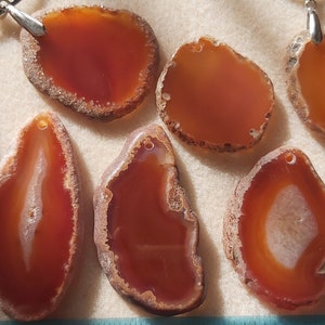 May include: A collection of eight agate slices in a variety of shapes and sizes. The agate slices are a mix of brown, orange, and white colours. The slices are all polished and have a smooth surface.