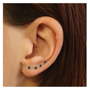 May include: A gold ear cuff with five blue gemstones set in a curved line.