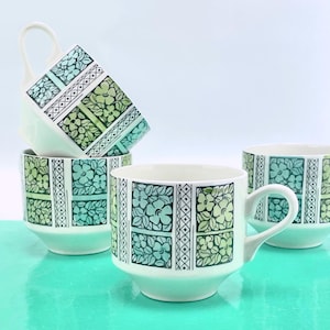 May include: Four white ceramic mugs with a floral design in shades of green and teal. The design is arranged in rectangular blocks with a white and black border. Each mug has a curved handle.
