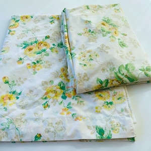 May include: White bed sheets with a floral pattern featuring yellow and peach roses, green leaves, and small yellow flowers. The sheets are folded and laid out, showcasing the detailed design.