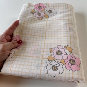 May include: A white fabric with a grid pattern and pink and white floral designs. The fabric has a subtle yellow hue.