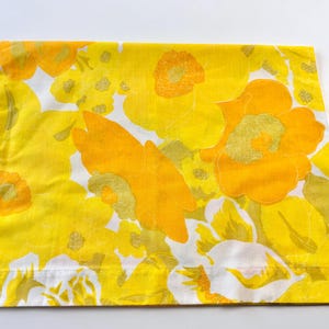 May include: A folded sheet with a vibrant floral pattern. The design features large, stylized flowers in shades of yellow and orange against a white background. The sheet is made of a soft, likely cotton, fabric.