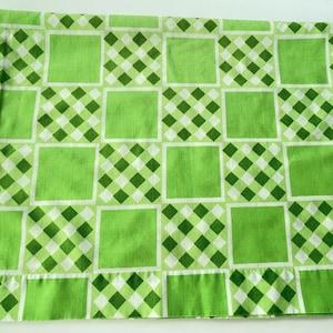 May include: A green and white patterned pillowcase. The pillowcase features a repeating pattern of large green squares alternating with smaller squares of green and white checkered designs. The fabric is a light, soft material.