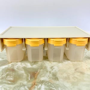 May include: A white plastic spice rack with four clear glass jars with yellow lids. The jars are empty.