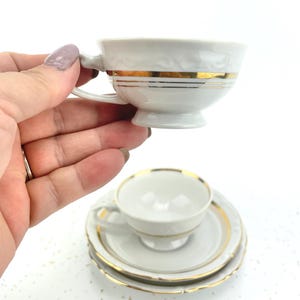 以下が含まれることがあります： 金色のトリムが付いた白い磁器のティーカップと、お揃いのソーサーセット。 ティーカップには小さなハンドルと、中央に装飾的な金色のバンドが付いています。 ソーサーにも金色のトリムが付いています。