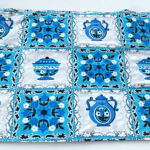 Puede incluir: Una tela rectangular con un patrón repetido de teteras azules, diseños florales y fuentes para servir sobre un fondo blanco. La tela tiene una combinación de colores azul claro y blanco.