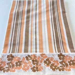May include: A folded textile with vertical stripes in shades of brown, peach, and white. The bottom edge features a border of floral designs in matching colors. The fabric appears to be cotton or a similar material.